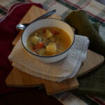 Bowl of potato soup on a cutting board with a spoon and towels
